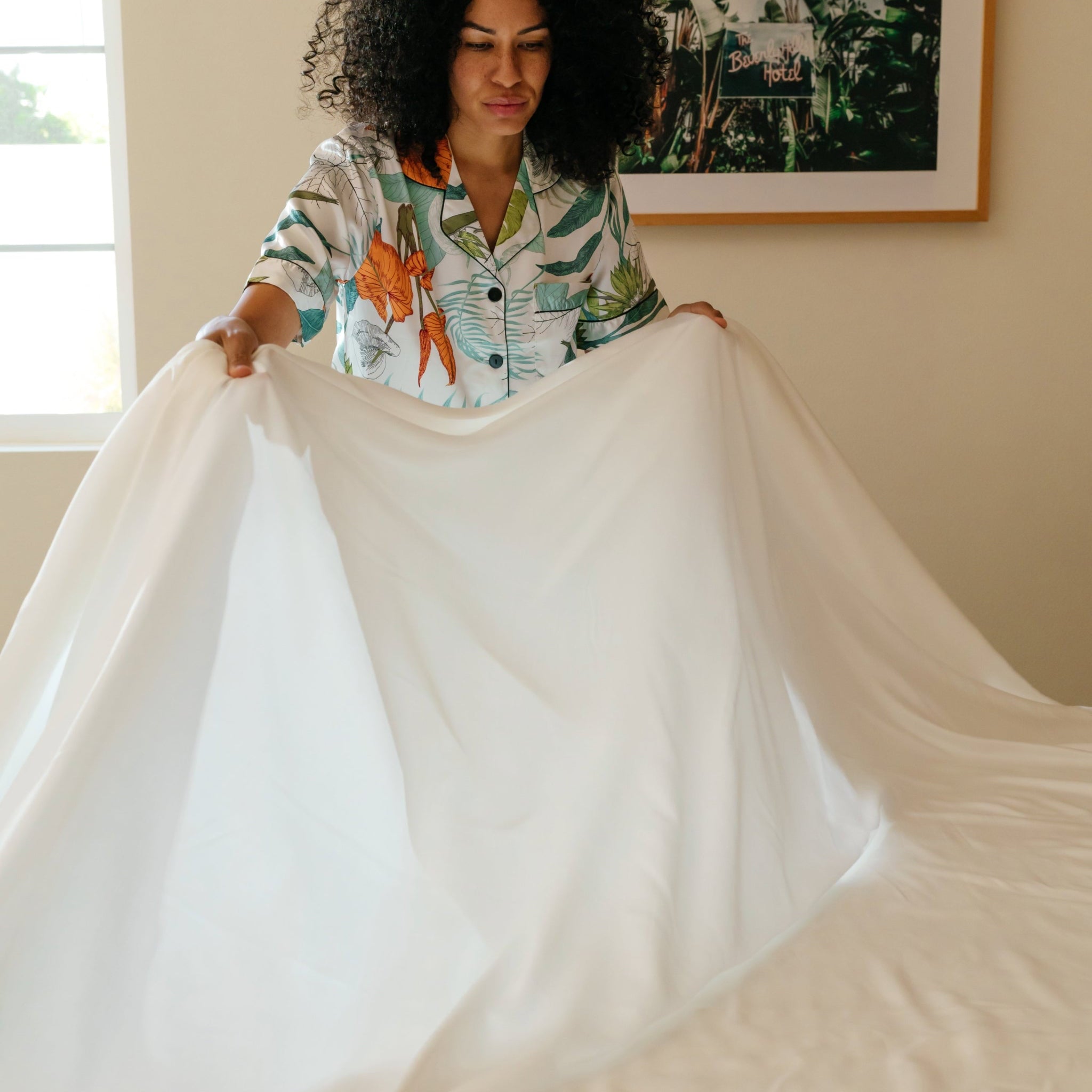 A person presenting an ivory white sateen sheet set, displaying the fabric's texture and color.